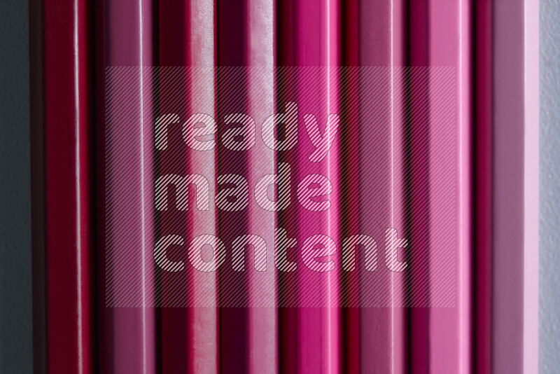 A collection of sharpened colored pencils arranged showcasing a gradient of pink hues on grey background