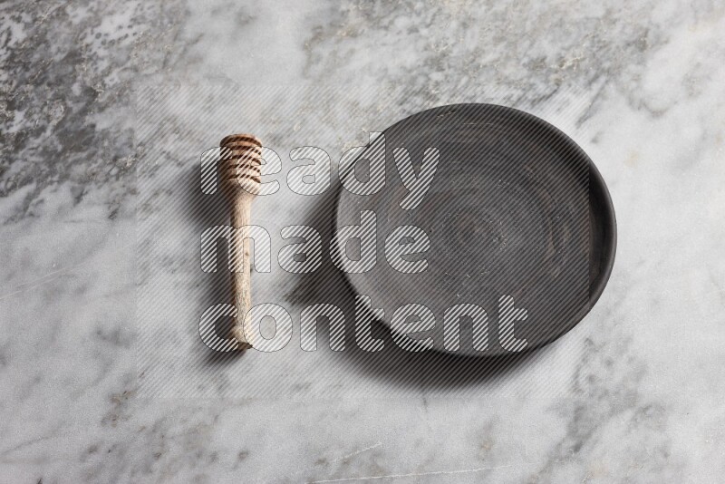 Black pottery plate with wooden honey dipper on the side on grey marble background