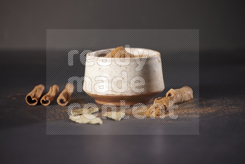 Cinnamon powder in a white pottery bowl and cinnamon sticks and laurel leaves on black background
