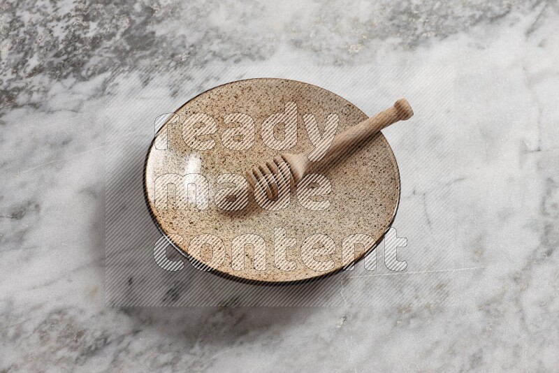 Multicolored pottery plate with wooden honey dipper in it on grey marble background