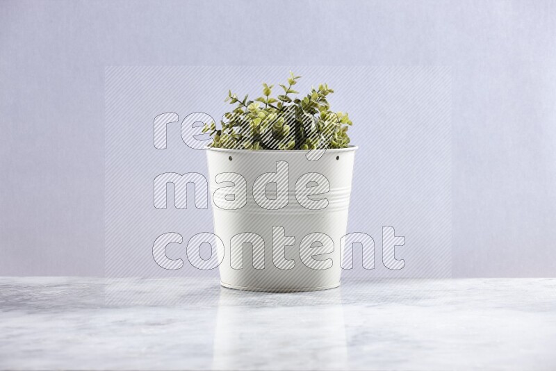Green artificial plant in white pot on grey marble background