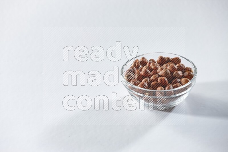 A glass bowl full of peeled hazelnuts on a white background in different angles