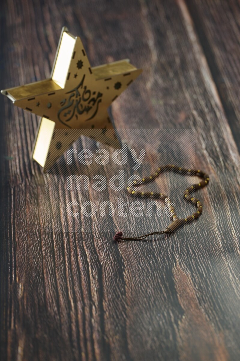 A wooden golden star lantern with different drinks, dates, nuts, prayer beads and quran on brown wooden background