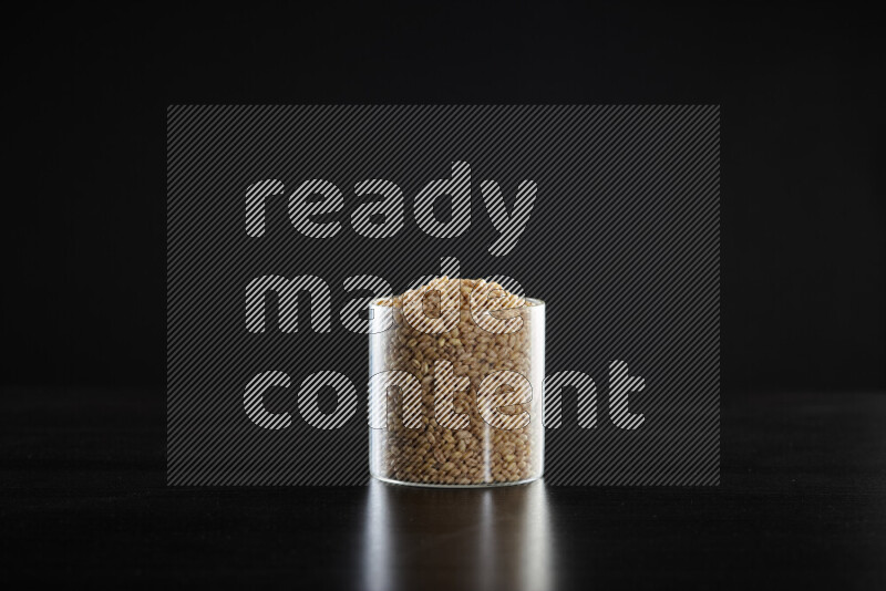 Hulled wheat in a glass jar on black background