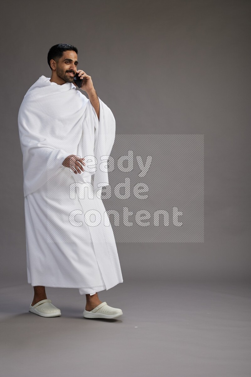 A man wearing Ehram Standing talking on phone on gray background