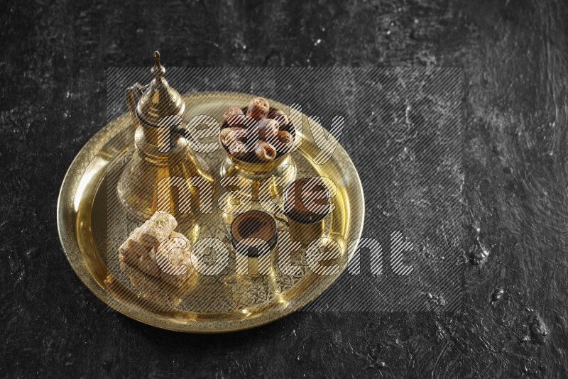 Oriental sweets with dates and a drink on a metal tray in a dark setup