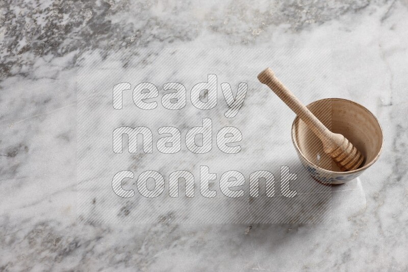 Decorative pottery bowl with wooden honey dipper in it on grey marble background