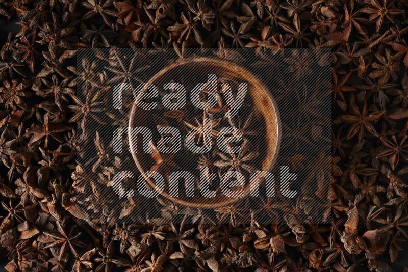 Star Anise in a wooden bowl and surrounded by more anise filling the frame on black flooring