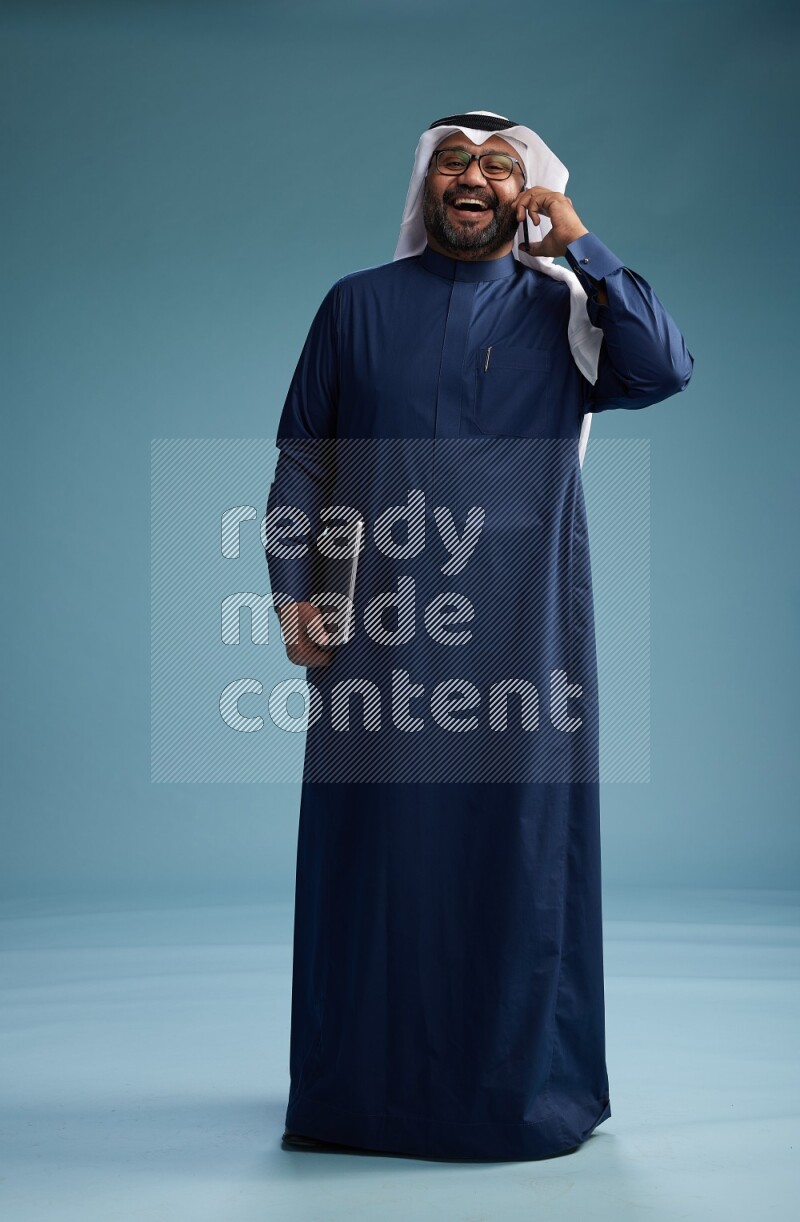 Saudi Man with shimag Standing talking on phone on blue background