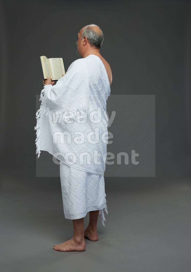 A man wearing Ehram Standing reading quran on gray background