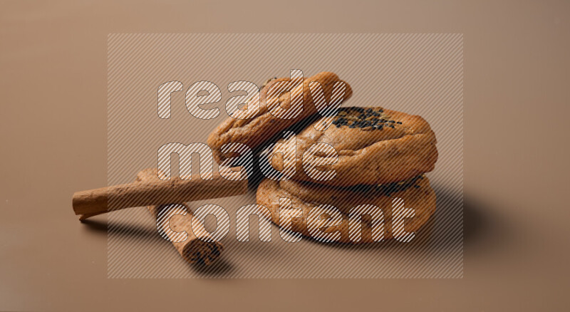 Three chocolate chip cookies beside cinimon sticks on a brown background