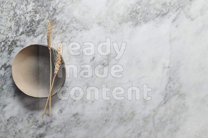 Wheat stalks on multicolored pottery plate on grey marble background