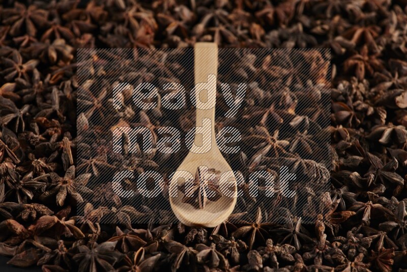Star Anise in a wooden spoon on more stars anise filling the frame on black flooring