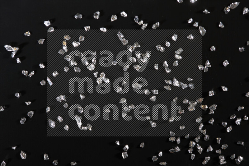Silver shimmering fragments of glass scattered on a black background