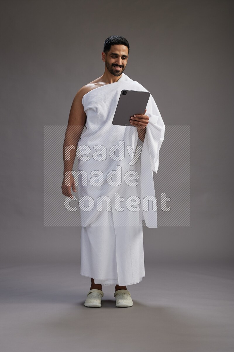 A man wearing Ehram and holding a tablet on gray background