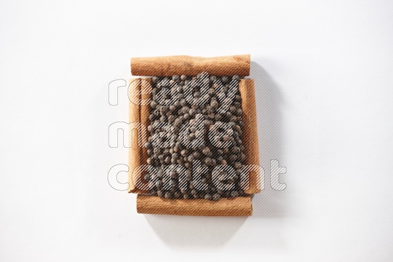 A single square of cinnamon sticks full of black pepper on white flooring