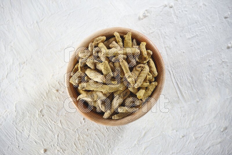 A wooden bowl full of dried turmeric whole fingers on a textured white flooring