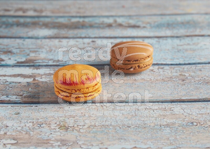 45º Shot of of two assorted Brown Irish Cream, and Orange Exotic macarons on light blue background