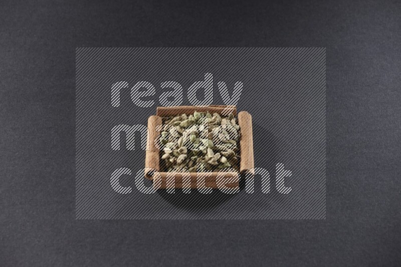 أربعة من أعواد القرفة مكونة شكل مربع بداخلها حبوب الهيل علي خلفية سوداء