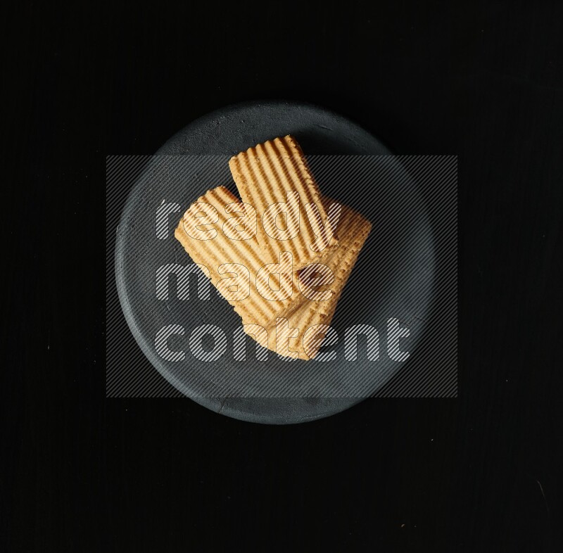 Golden biscuits in a black pottery plate on black background