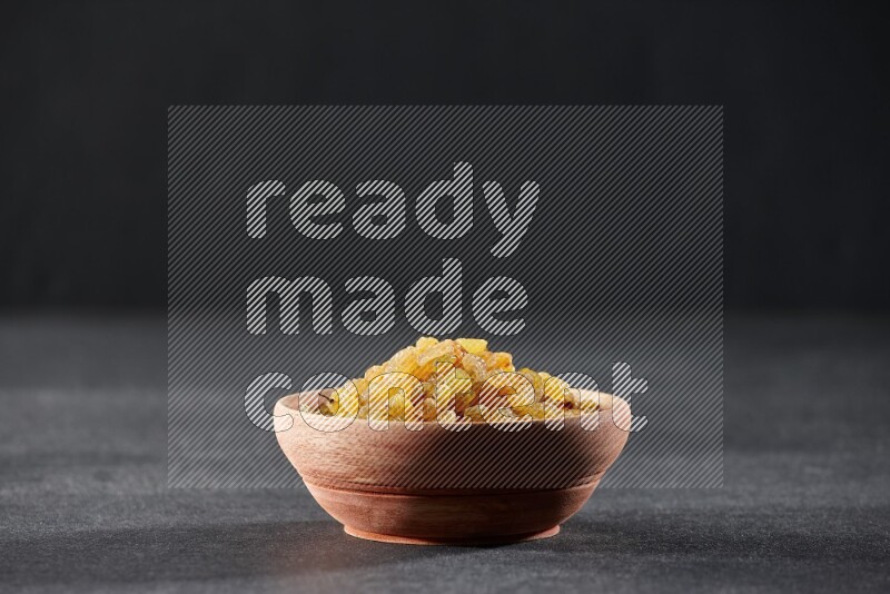 A wooden bowl full of raisins on a black background in different angles