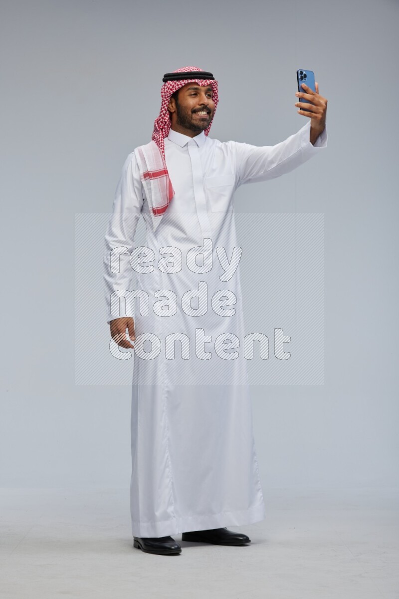 Saudi man Wearing Thob and shomag standing taking selfie on Gray background