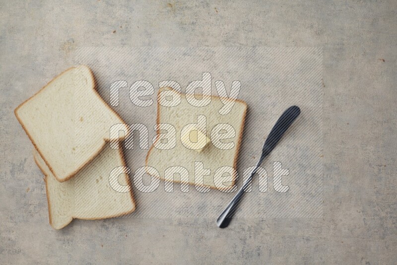 White toast slices with a butter cube and a spreading knife on a light blue textured background