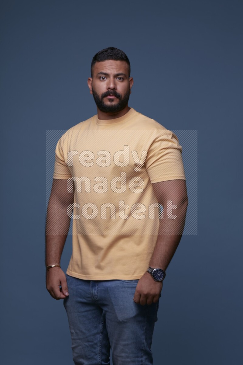 A man posing in a blue background wearing a yellow shirt