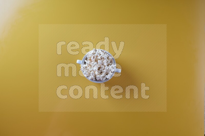 A white ceramic bowl full of popcorn on a yellow background in a top view shot