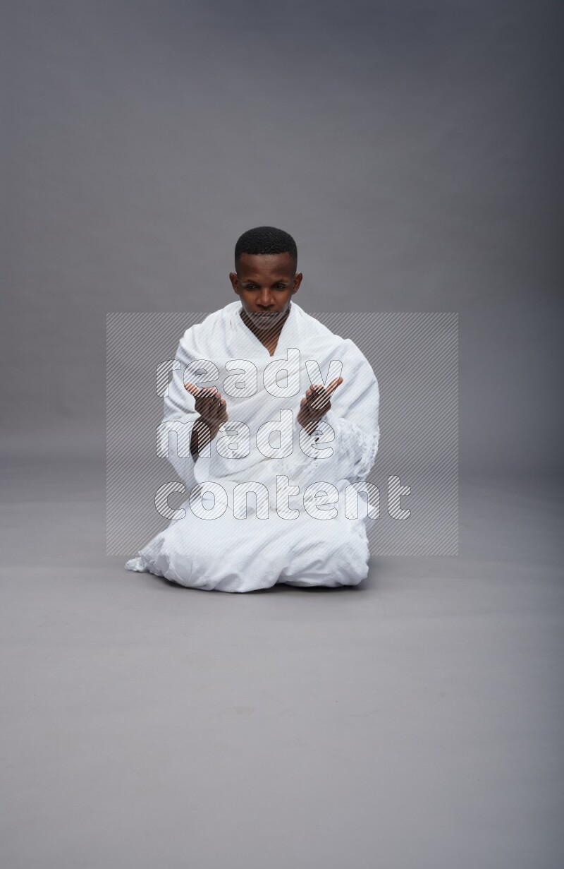 A man wearing Ehram sitting on floor dua'a on gray background