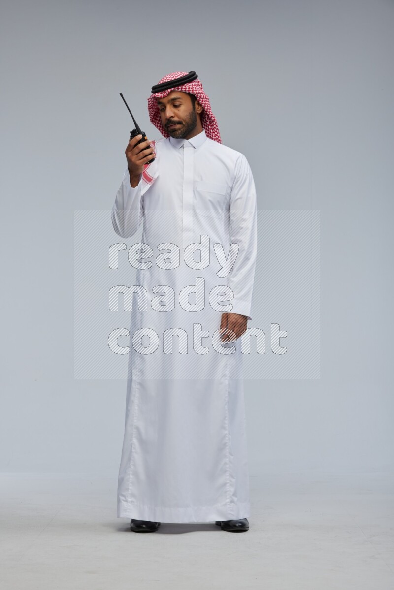 Saudi man Wearing Thob and shomag standing holding walkie-talkie on Gray background