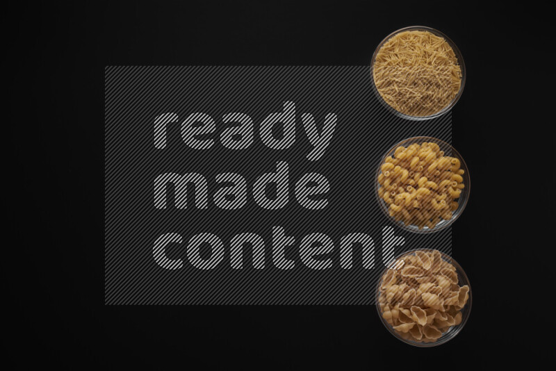 Different pasta types in 3 glass bowls on black background