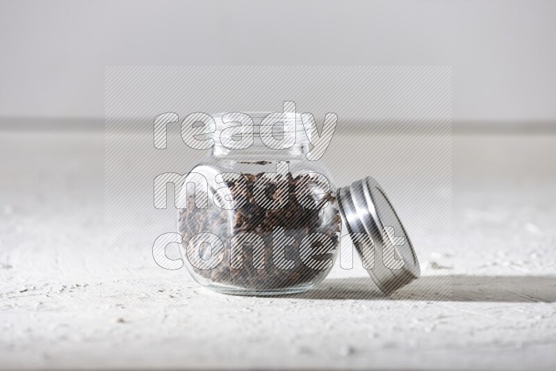 A glass spice jar full of cloves on textured white flooring