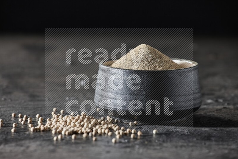 وعاء فخار أسود مملوء ببودرة الفلفل الأبيض مع حبات الفلفل الأبيض على أرضية سوداء