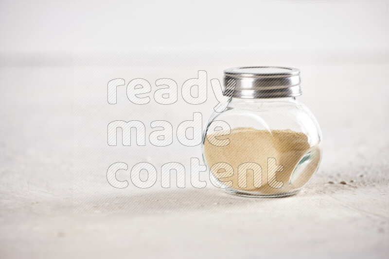 A glass jar full of ground ginger powder on white background