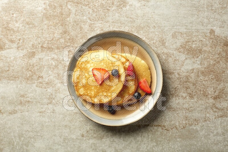 Three stacked mixed berries pancakes in a bicolor plate on beige background