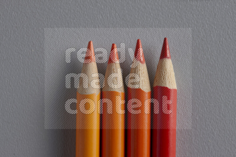 A collection of colored pencils arranged showcasing a gradient of orange hues on grey background
