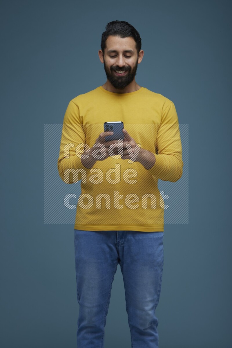Man typing on his phone in a blue background wearing a yellow shirt