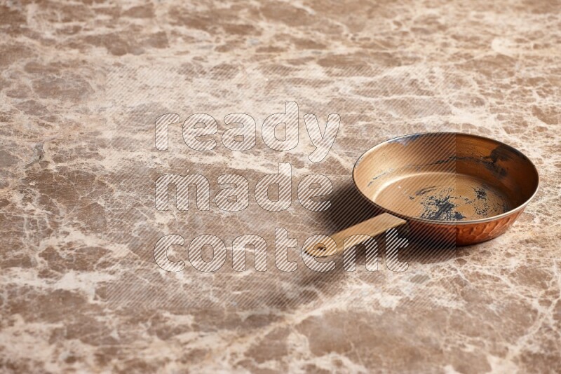 A small copper pan on beige marble background