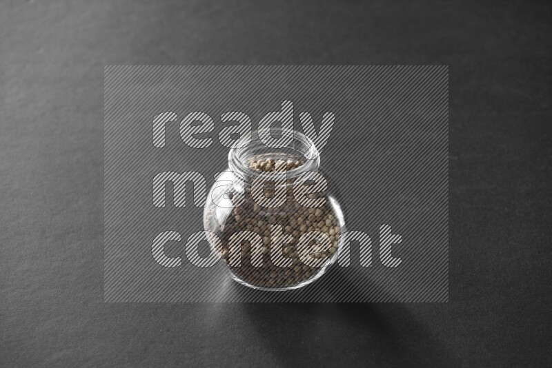 A glass spice jar full of white peppers on black flooring