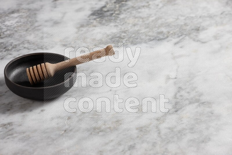 Black pottery bowl with wooden honey dipper in it on grey marble background