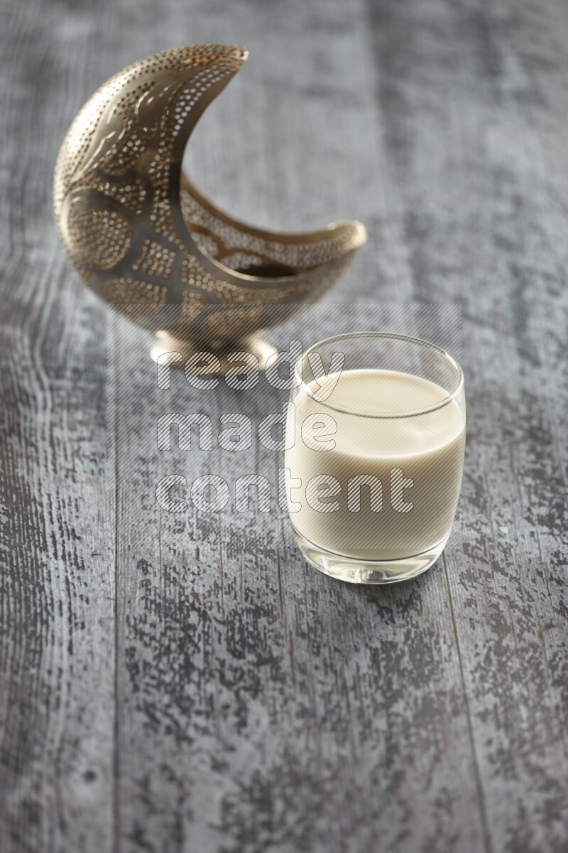 A silver lantern with different drinks, dates, nuts, prayer beads and quran on grey wooden background