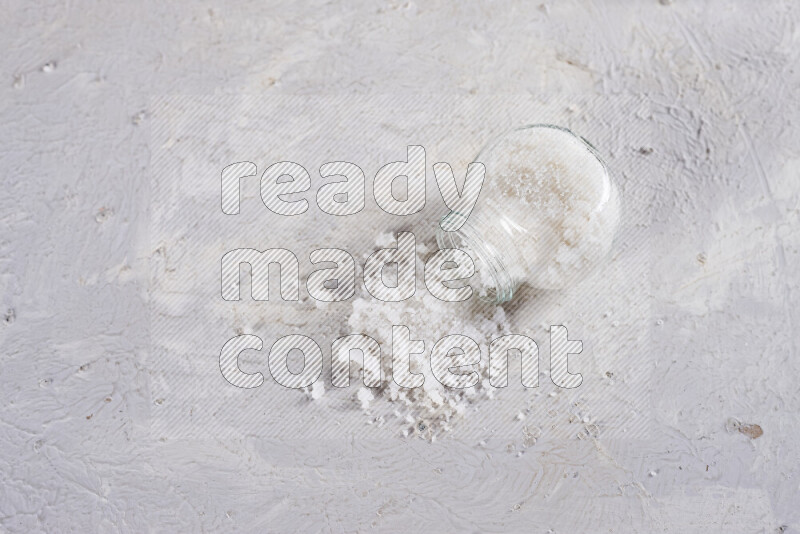 A glass jar full of coarse sea salt crystals on white background