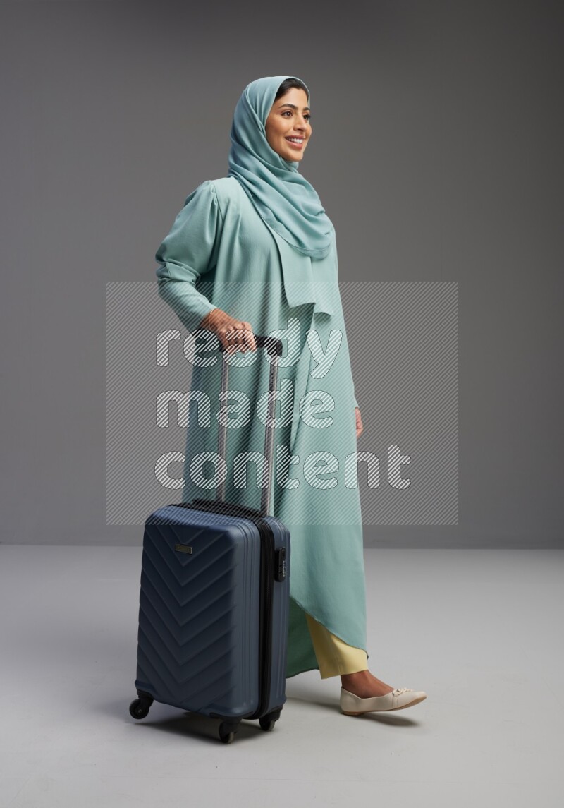 Saudi Woman wearing Abaya standing holding Travel bag on Gray background