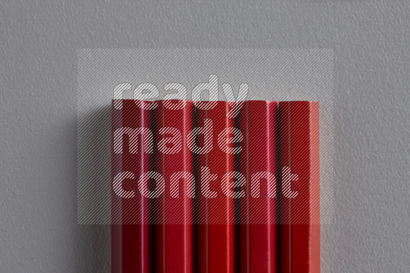 A collection of sharpened colored pencils arranged showcasing a gradient of red hues on grey background