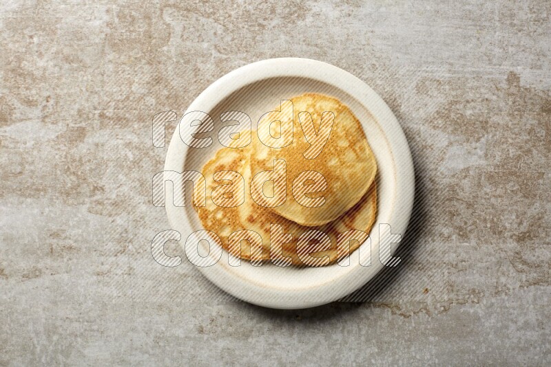 Three stacked plain pancakes in a beige plate on grey beige background