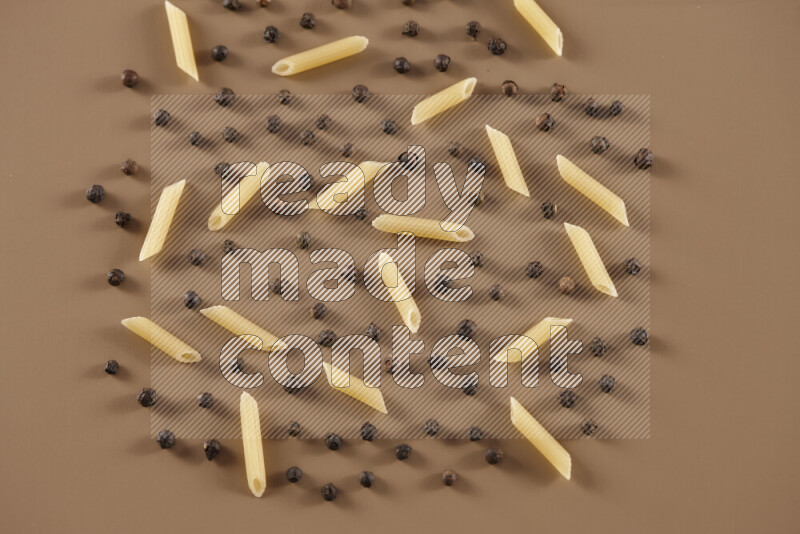 Raw pasta with different ingredients such as cherry tomatoes, garlic, onions, red chilis, black pepper, white pepper, bay laurel leaves, rosemary and cardamom on beige background