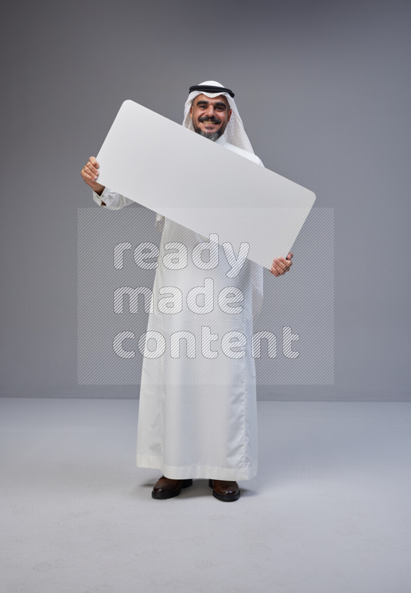Saudi man Wearing Thob and white Shomag standing holding board on Gray background