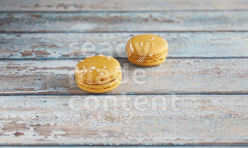 45º Shot of two Yellow Piña Colada macarons on light blue wooden background