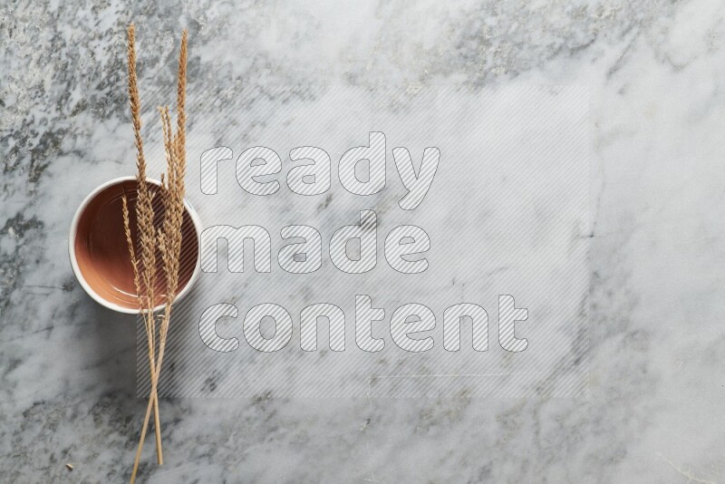 Wheat stalks on brown pottery bowl on grey marble background